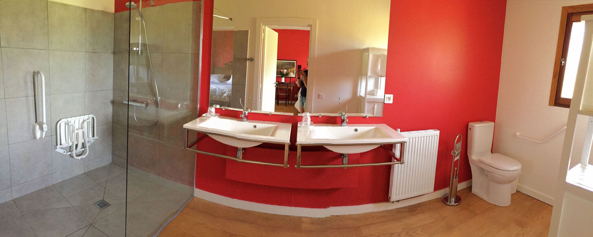 A modern bathroom with a glass shower enclosure, two sinks, a toilet, and a red accent wall.