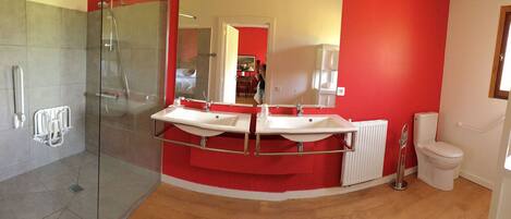 A modern bathroom with a glass shower enclosure, two sinks, a toilet, and a red accent wall.