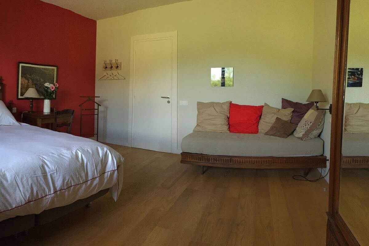 A bedroom with a large bed, a sofa, a wooden headboard, a red wall, and a door.