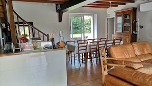 A kitchen with a central island, wooden chairs, a brown leather sofa, and a dining table. - Gîtes LES Fougeres DU LAC (Saint-Plantaire)