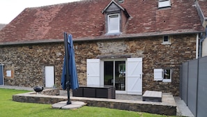A stone building with a red-tiled roof, a covered patio area with outdoor furniture, and a grassy yard. - Gîtes LES Fougeres DU LAC (Saint-Plantaire)