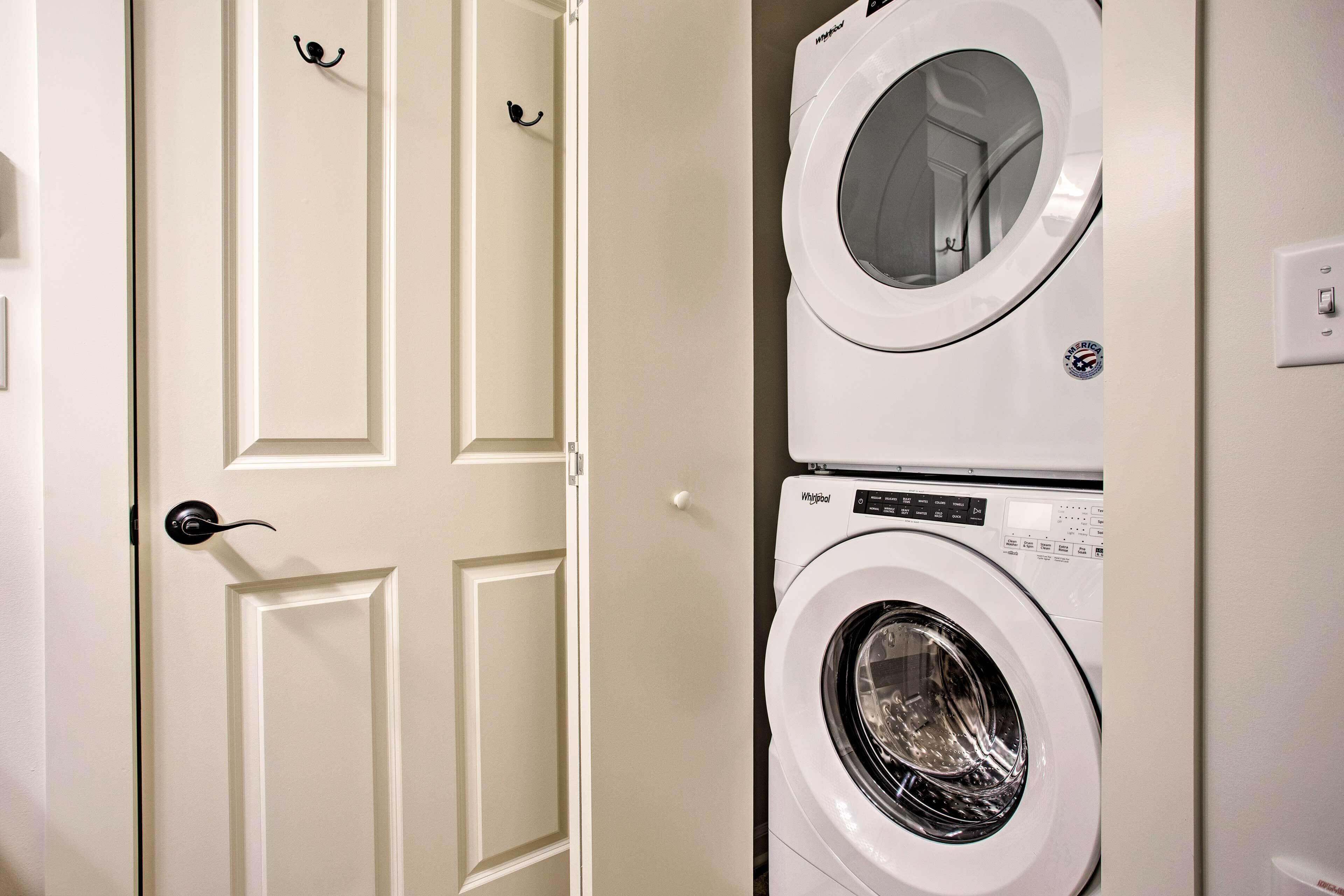 Une buanderie équipée d’un lave-linge et d’un sèche-linge superposés, d’une porte blanche avec une poignée noire et d’un interrupteur sur le mur.