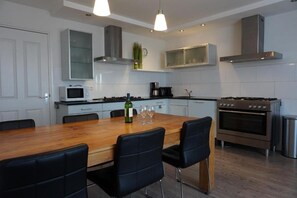 A modern kitchen with a wooden dining table, black chairs, a built-in oven, and stainless steel appliances.