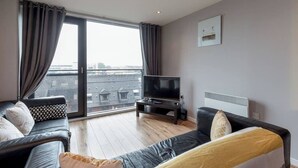 A modern living room with a sofa, a television, and a large window with curtains. - Close to Hydro/SECC: Modern Riverside Apt with Parking (Glasgow City)
