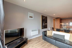 A modern living room with a flat-screen TV, a leather sofa, a dining area, and a kitchen in the background. - Close to Hydro/SECC: Modern Riverside Apt with Parking (Glasgow City)