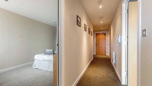 A hotel hallway with a carpeted floor, a bed with white bedding, and a wooden door at the end. - Close to Hydro/SECC: Modern Riverside Apt with Parking (Glasgow City)