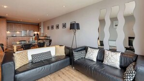 A modern living room with a black leather sofa, a dining area, and a kitchen in the background. - Close to Hydro/SECC: Modern Riverside Apt with Parking (Glasgow City)