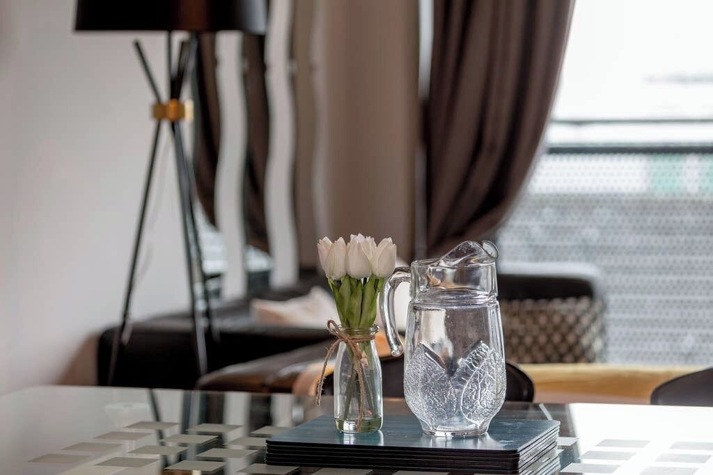 Ein klarer Glasbehälter und eine Vase mit weißen Blumen auf einem Tisch mit geometrischem Muster.