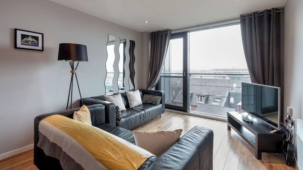 A modern living room with a sofa, a TV, and a large window with curtains. - Close to Hydro/SECC: Modern Riverside Apt with Parking (Glasgow City)