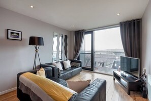 A modern living room with a sofa, a TV, and a large window with curtains. - Close to Hydro/SECC: Modern Riverside Apt with Parking (Glasgow City)