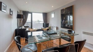 A modern hotel room with a glass dining table, black leather chairs, a sofa, a TV, and a large abstract painting. - Close to Hydro/SECC: Modern Riverside Apt with Parking (Glasgow City)