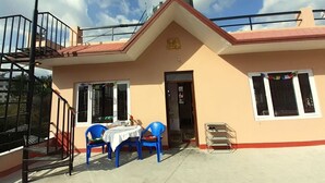 A two-story building with a red roof, a balcony with a metal railing, and a table with blue plastic chairs outside. - A Dutch Nepali home with a beautiful view (kathmandu)