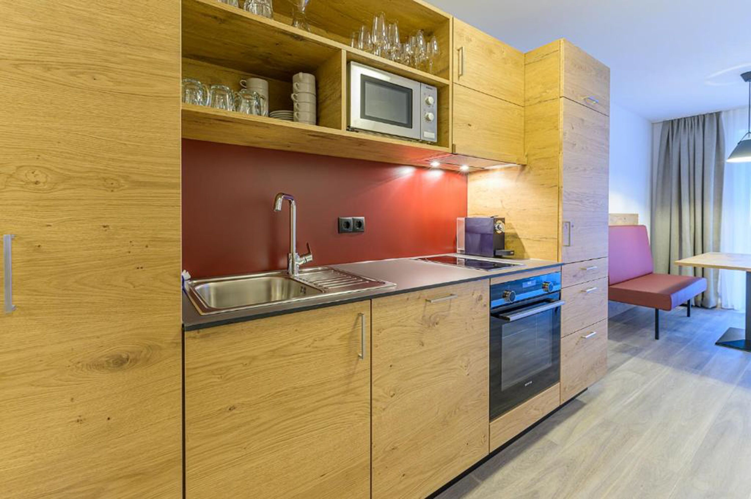 A modern kitchen with wooden cabinets, a stainless steel sink, a microwave, and a built-in oven.