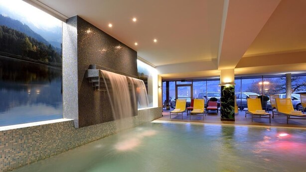 A spa area with a waterfall feature, a pool, and several lounge chairs. - Residenz Schiestl (Fuegenberg)