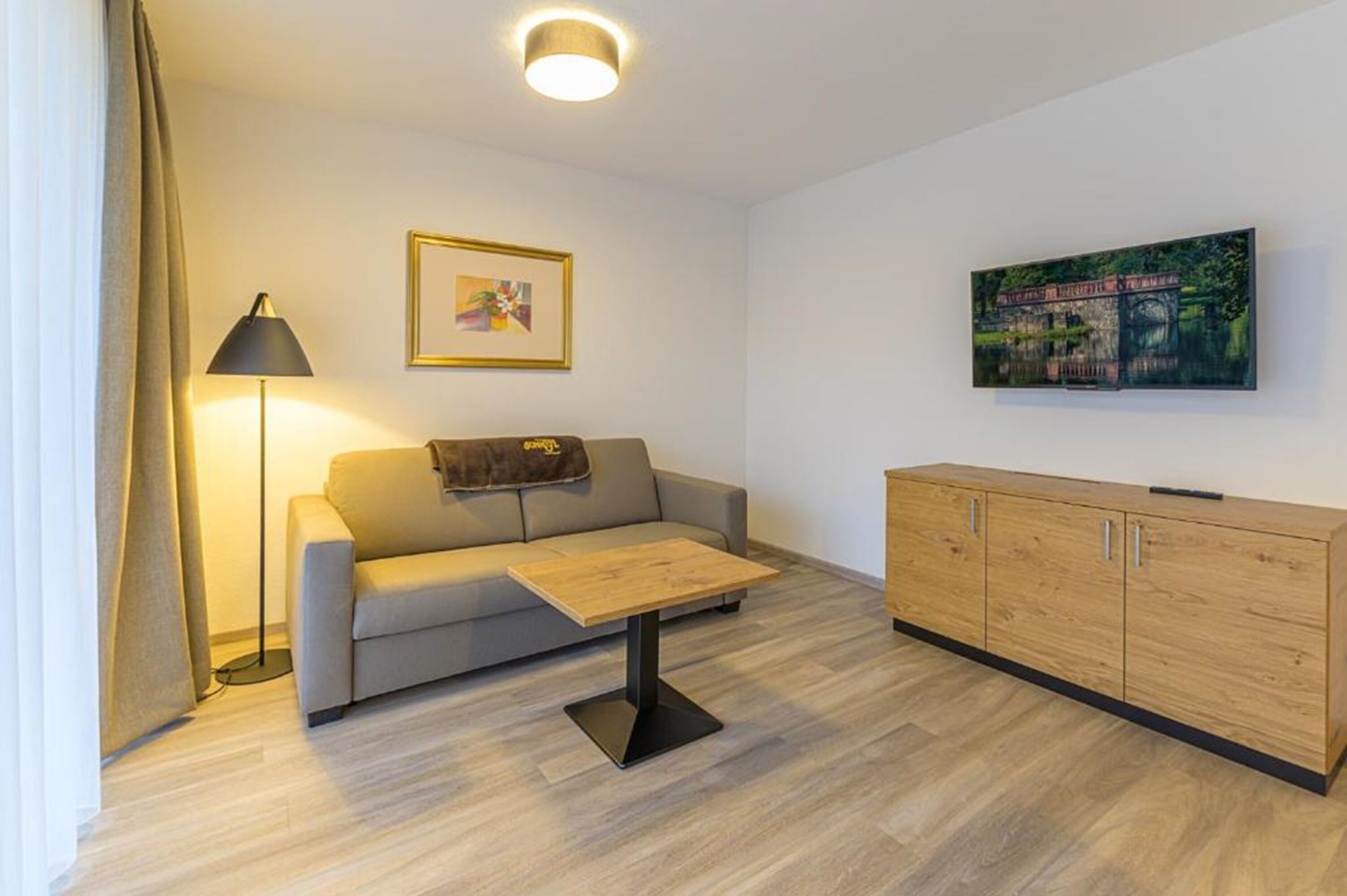 Un salon moderne comprenant un canapé, une table basse, un lampadaire, un meuble et deux œuvres d’art encadrées accrochées au mur.