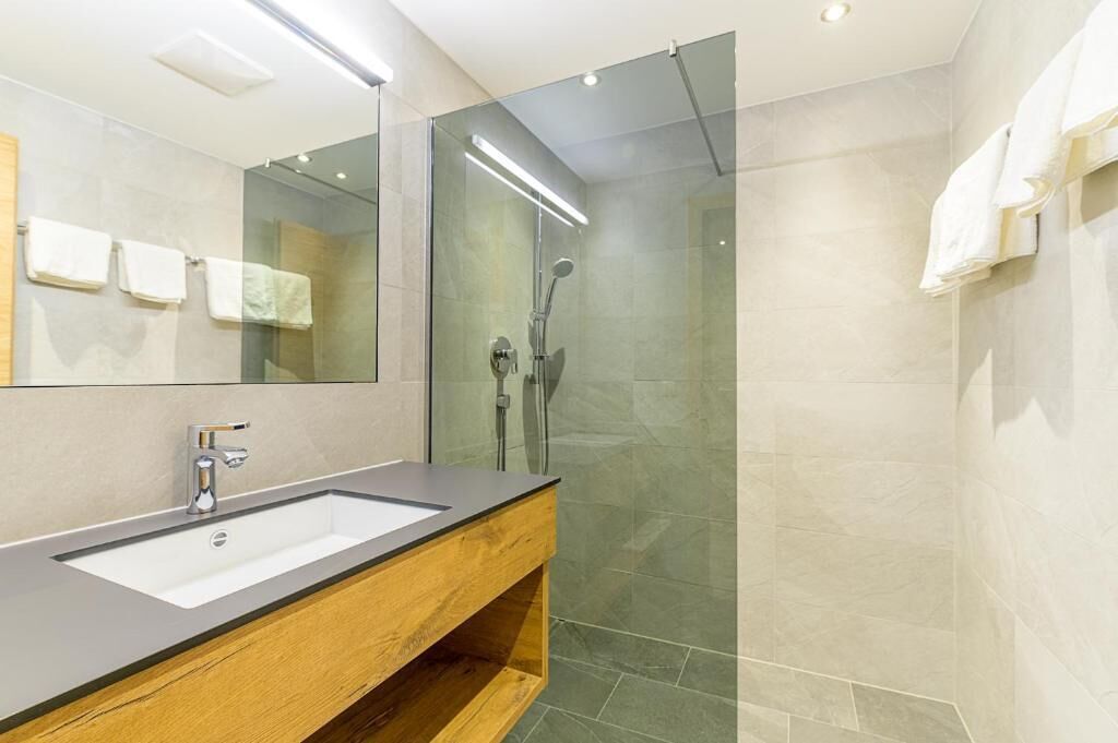 A modern bathroom with a large mirror, a wooden vanity, a glass-enclosed shower, and a tiled floor.