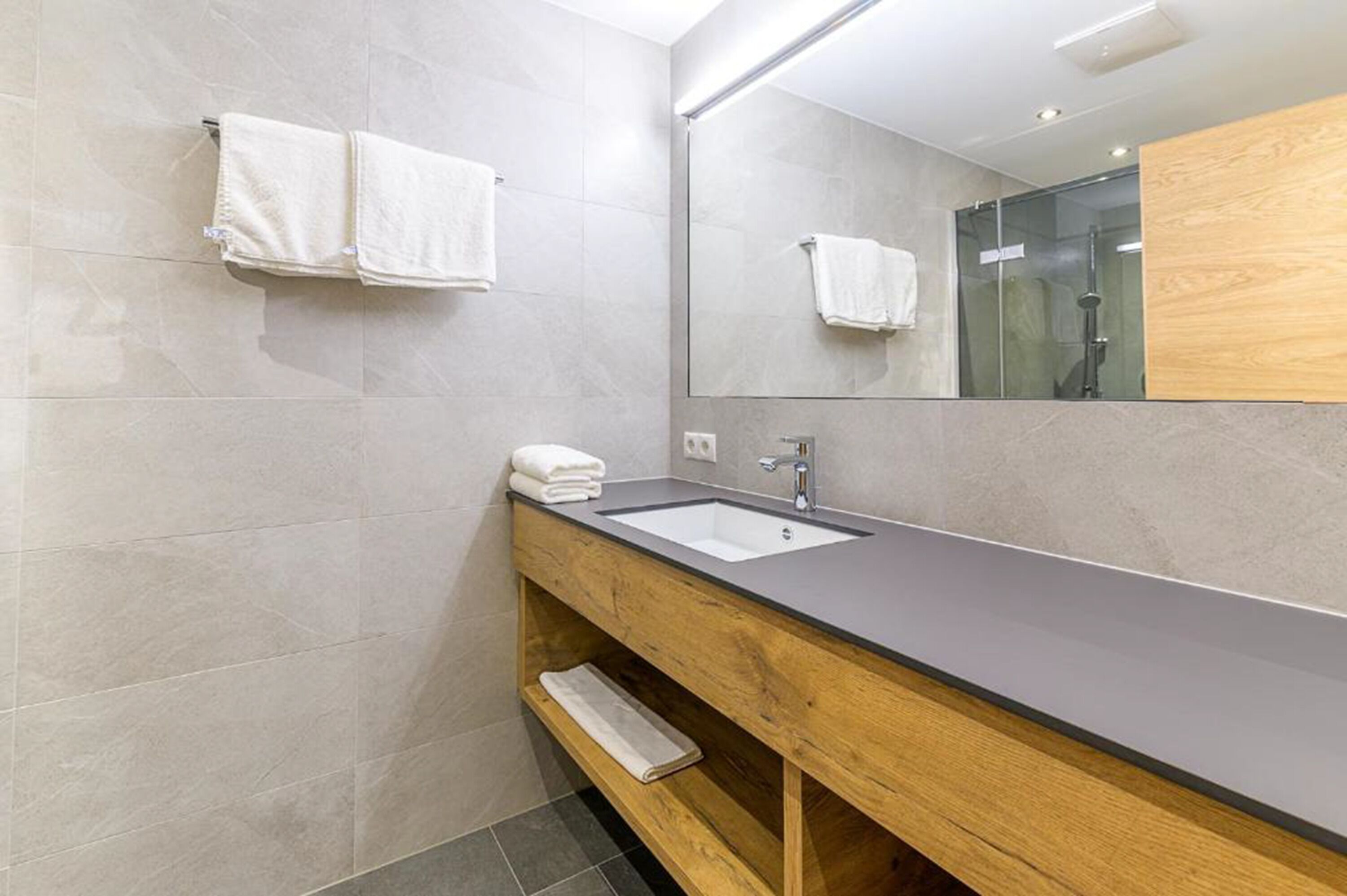 A modern bathroom with a wooden vanity, a sink, and a large mirror.