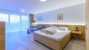 A modern hotel room with a wooden bed, a desk, and a chair. There are two framed pictures on the wall and a window with curtains. - Residenz Schiestl (Fuegenberg)