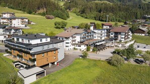 A modern hotel complex with multiple buildings, a parking area, and a view of the surrounding green landscape and hills. - Residenz Schiestl (Fuegenberg)