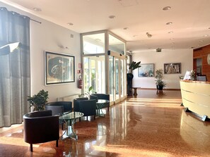 A hotel lobby with a reception desk, seating area with chairs and tables, and a large glass door leading to the outside. - Hotel Riverside (San Cesario sul Panaro)
