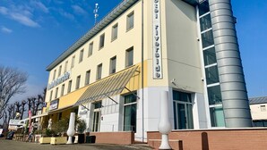 Ein Hotel mit modernem Design, das ein markantes Schild 'Hotel Riverside', eine Straßencafé und eine große zylindrische Struktur an der Ecke zeigt.