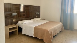 Ein Schlafzimmer mit einem Holz-Kopfteil, zwei Nachttischen, einem Bett mit weißer Bettwäsche, einer beigen Tagesdecke und einem Fenster mit blauen Vorhängen.