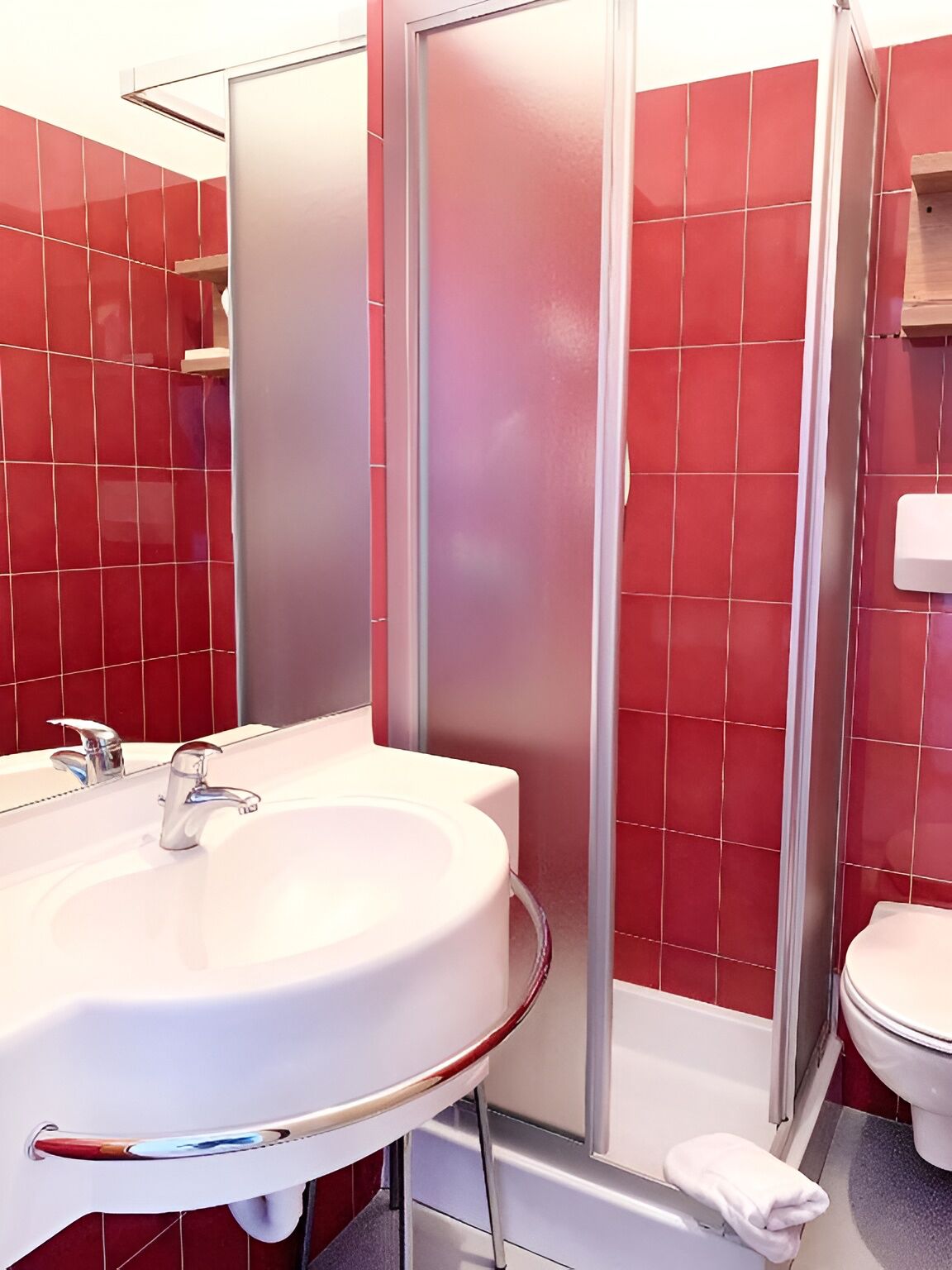 Un baño con lavamanos blanco, cabina de ducha con mampara de vidrio y retrete.