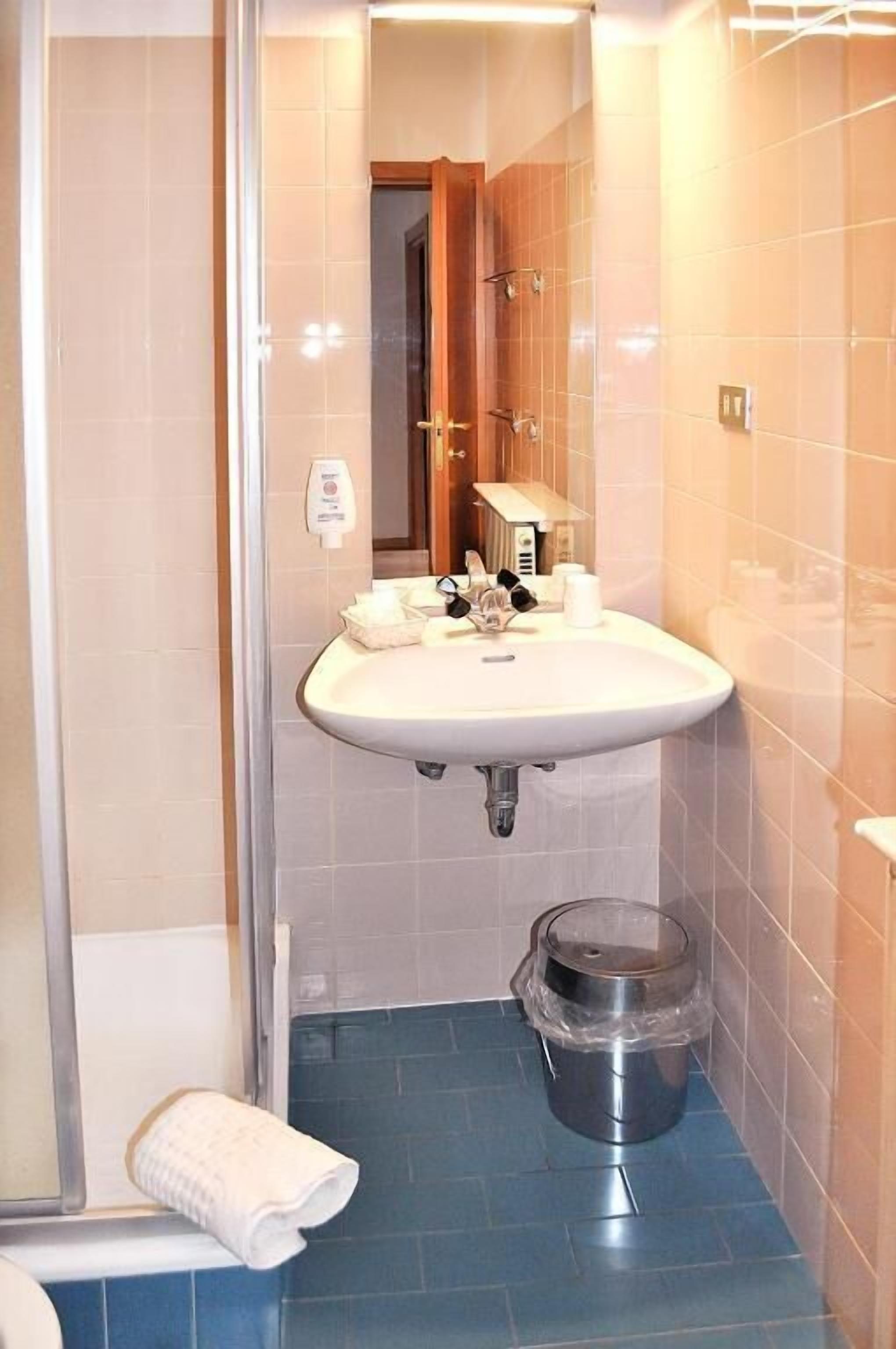 A bathroom with a sink, mirror, and a trash bin.