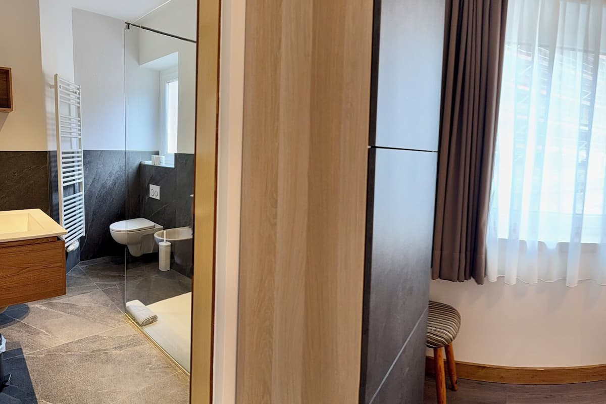 Hotelkamer met een bed, nachtkastje, spiegel, raam met gordijnen, houten hoofdeinde en een wandlamp.