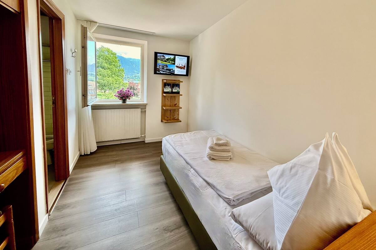 Een kamer met een bed, een raam met uitzicht, een radiator en een televisie aan de muur.