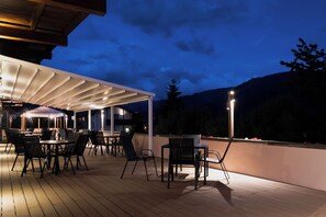 Une terrasse extérieure avec des tables et des chaises, un espace salon couvert et une vue sur les montagnes.