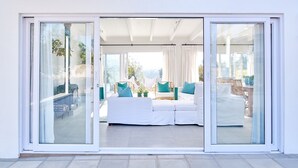 Ein modernes Interieur mit einer weißen Sofagarnitur, einem Holzstuhl und einem Essbereich, der durch große Glasüren sichtbar ist.