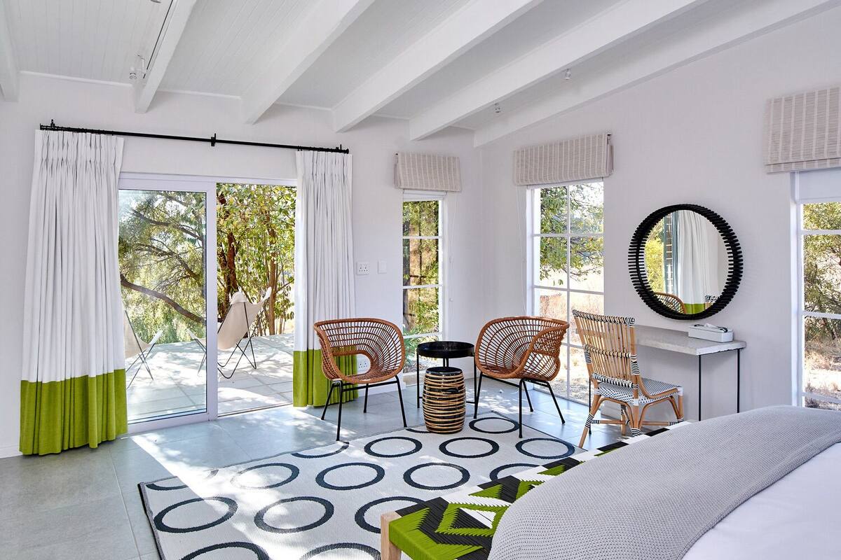 Un dormitorio moderno con una cama grande, un escritorio y dos sillones de mimbre.