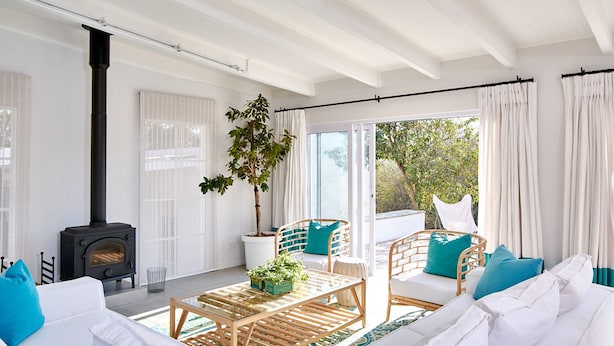 Ein modernes Wohnzimmer mit einem schwarzen Kaminofen, weißen Möbeln und einem großen Fenster mit Blick auf Grünflächen.