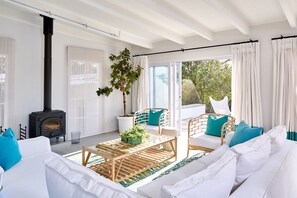 Sala moderna com lareira a lenha preta, móveis brancos e uma janela ampla com vista para o verde.