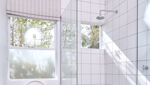 Ein modernes Badezimmer mit Toilette, einer Duschkabine aus Glas und einem Fenster mit Blick auf Bäume.