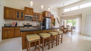 A spacious kitchen with wooden cabinets, a central island with bar stools, and a large window providing natural light. - Contemporary Design With Lots of big Windows (Sosúa)