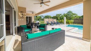 A covered outdoor area with wicker furniture, a pool, and a patio with a view of greenery. - Contemporary Design With Lots of big Windows (Sosúa)