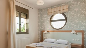 A bedroom with a bed, two bedside tables, a window with blinds, a radiator, and a wall with a floral pattern. - Countryside villa with private pool and views (Rethimno)