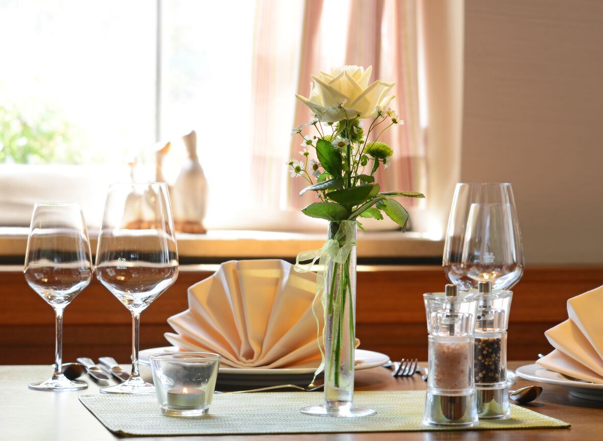 A dining table set with wine glasses, a candle, salt and pepper shakers, and a vase with a white rose.