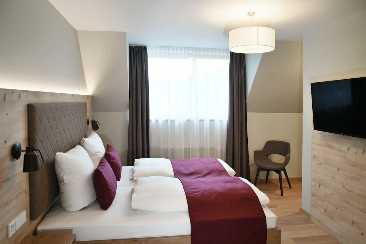 A modern hotel room with a large bed, a TV, a desk, and a chair.