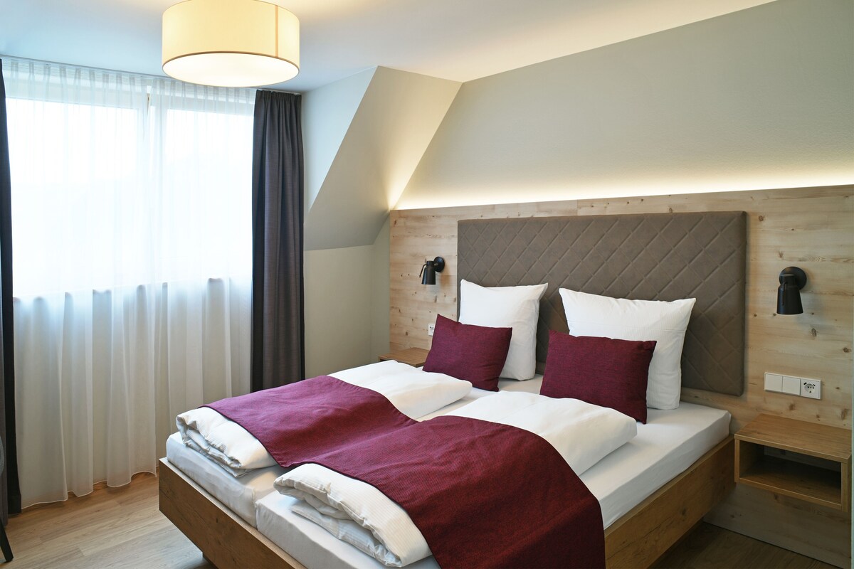 A double bed with a wooden headboard, white bedding, and a red throw blanket.
