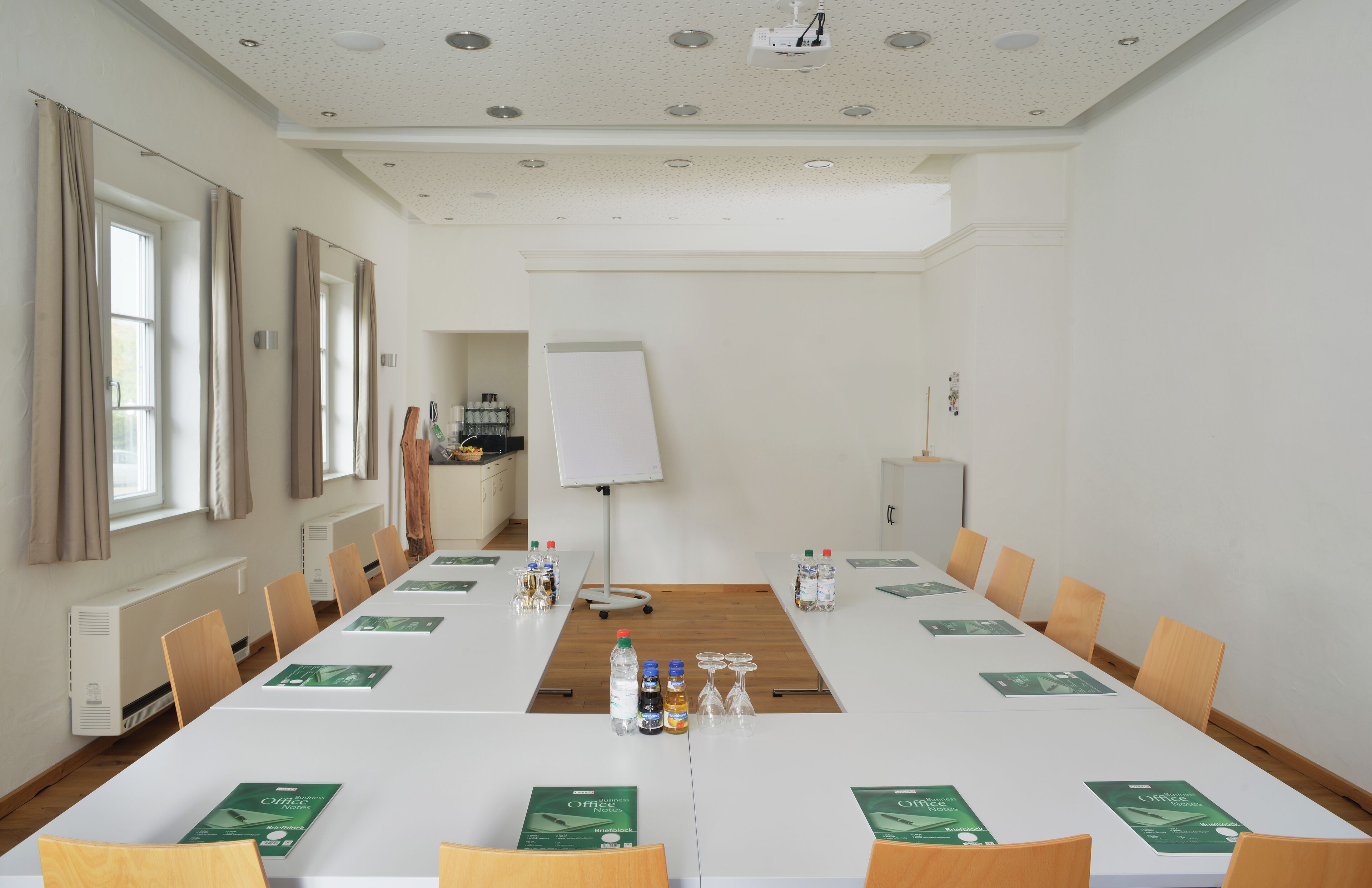 Una sala de conferencias con una larga mesa, sillas, una pizarra y un proyector.