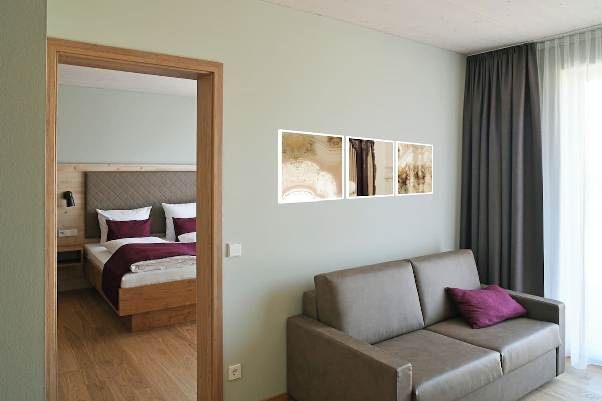 A modern hotel room with a bed, a sofa, and a large window with curtains.