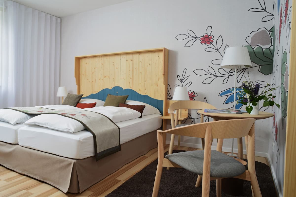 A hotel room with a bed, a chair, a small table, and a wall with a floral mural.