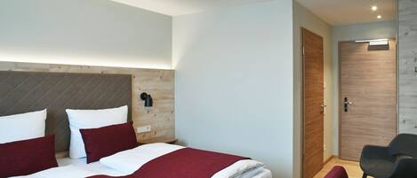 A modern hotel room with a large bed, a wooden headboard, a bedside table, a nightstand, a chair, and a wardrobe.