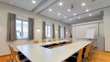 A conference room with a long table, chairs, a whiteboard, and windows with curtains.