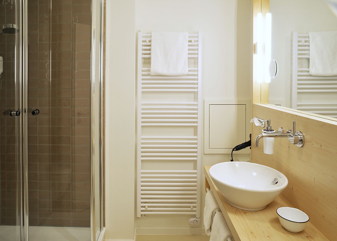 A modern bathroom with a glass shower enclosure, a white sink, and a towel rack.