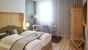 A hotel room with a bed, two chairs, a small table, a wooden cabinet, and a window with curtains. - Hotel & Restaurant Klosterhof (Gutenzell)