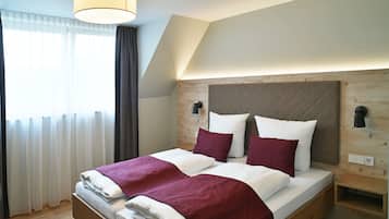 Een tweepersoonsbed met een houten hoofdbord, beddengoed in wit en rood, en een nachtkastje met een lamp.